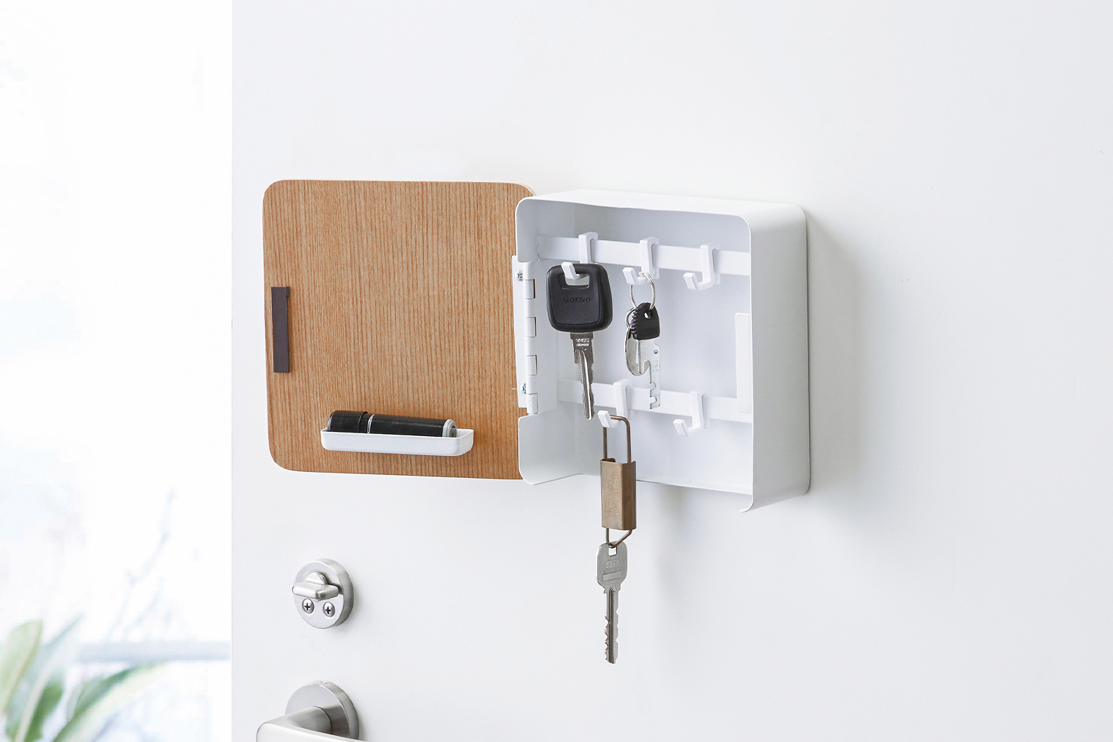 Yamazaki Home white Magnetic Key Hook Cabinet on a door holding three keys with hooks. 