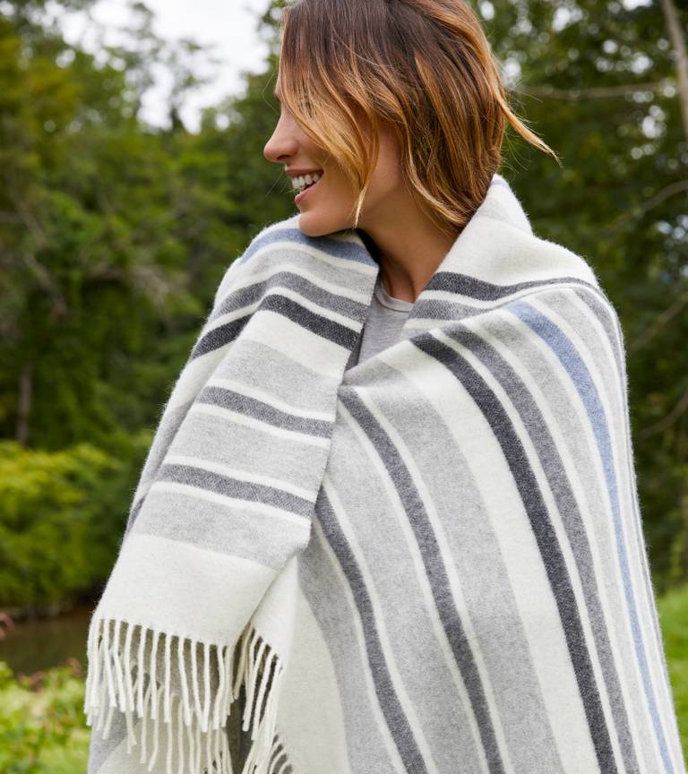Woman keeping warm with a white, grey, and light blue striped throw blanket draped over her shoulders