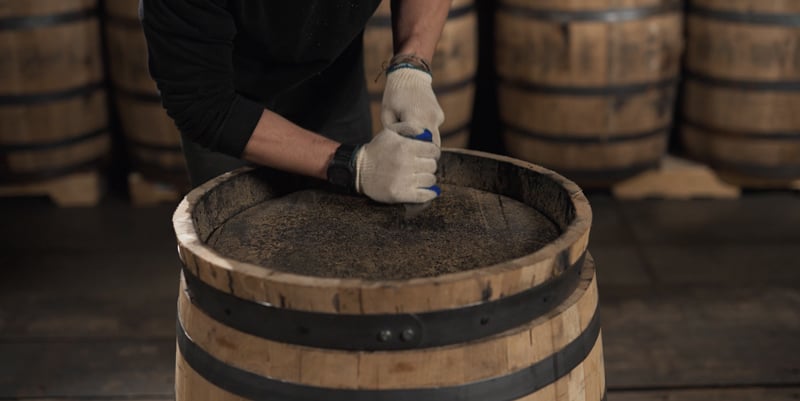 A person scrapes away char off the head of a used whiskey barrel.