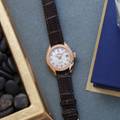 Grand Seiko wristwatch STGK006 - white dial, gold case on a brown strap atop a table. 