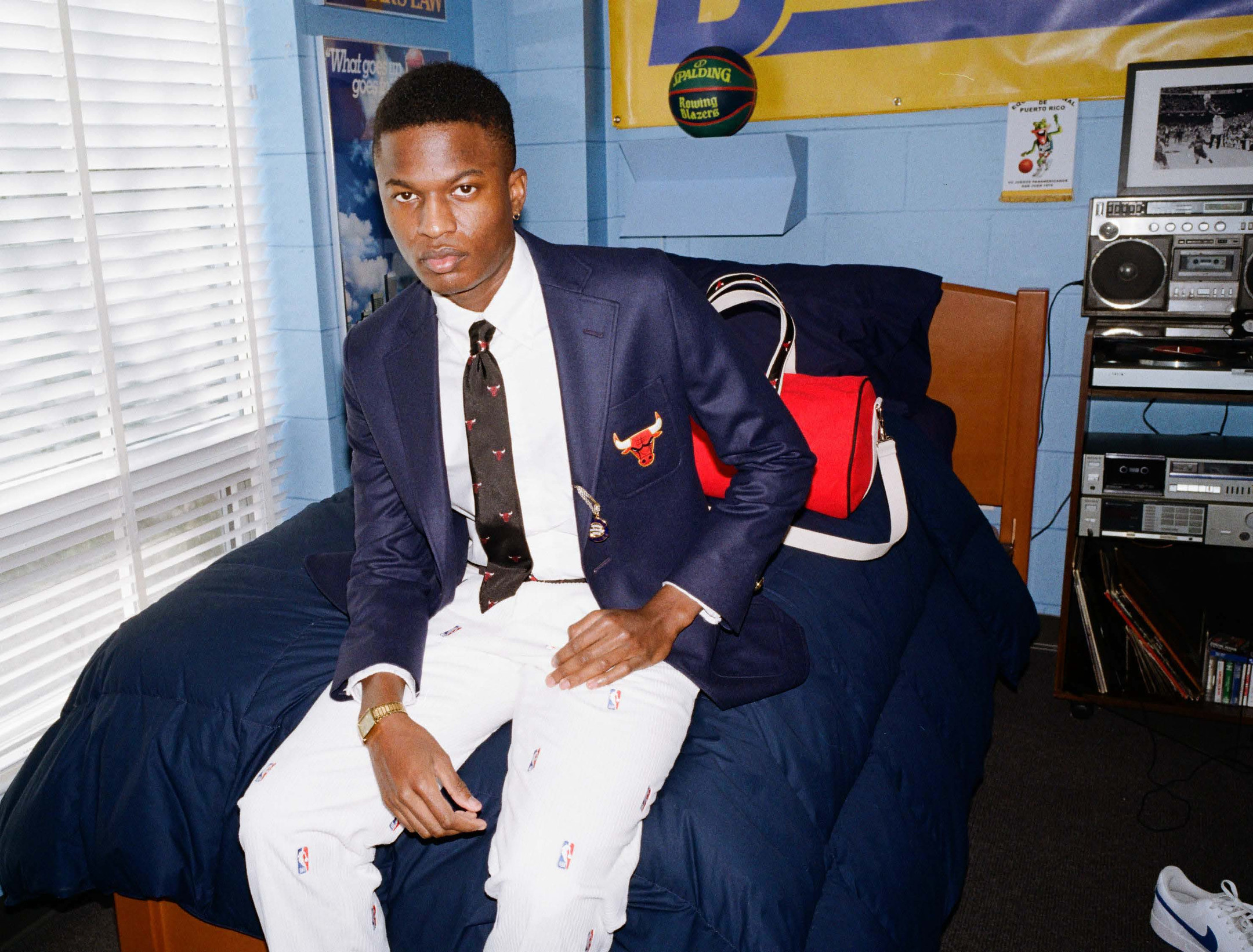 Model sitting on a bed in a dorm room, wearing the Chicago Bulls Tie, Blazer, and Belt.