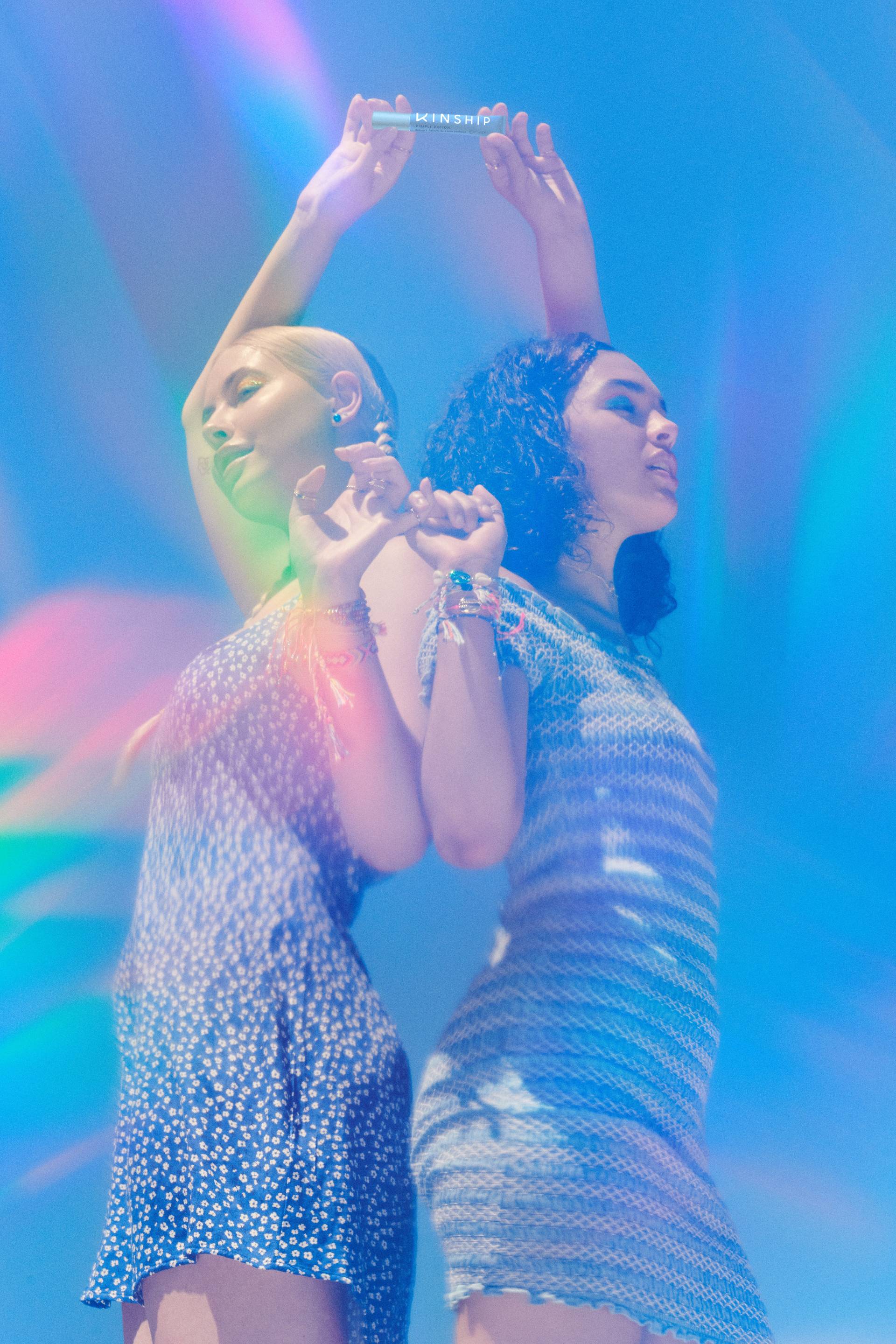 Two friends hold hands outdoors, cast in a rainbow prism of light 