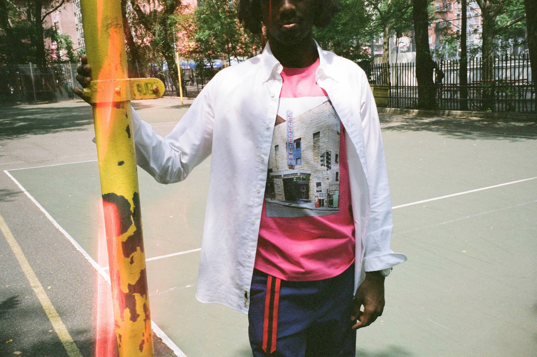 Male model wearing the Georgetown Theater Tee in pink, the Oxford Button-Down in white, the Navy Cotton Twill Wide Leg Trousers and the Grosgrain Belt in red and black
