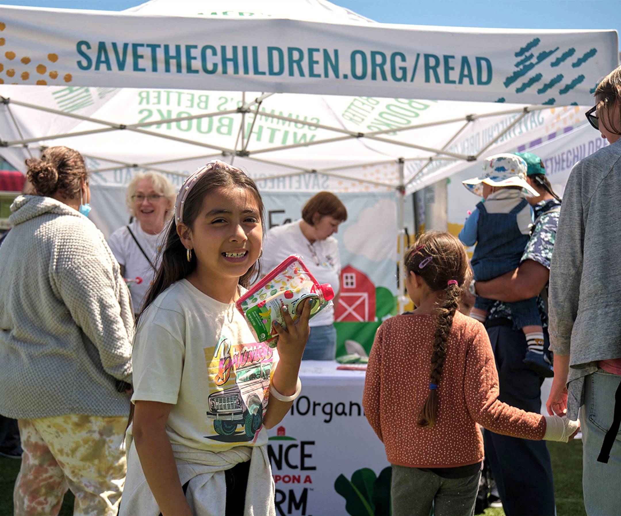 Image of a child holding a Once Upon a Farm pouch at a Save the Children event.